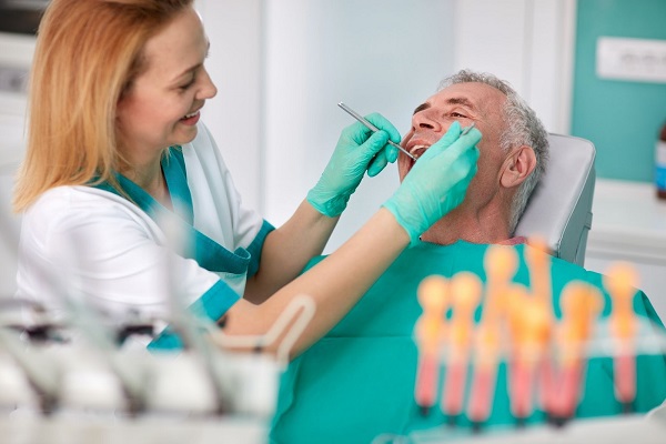 Dentist examining senior patient mouth with angled mirror and scaler during treatment