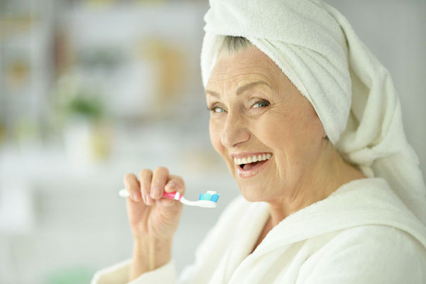 An Image of an elder woman brushing her teeth in the bathroom representing the healthy teeth concept.