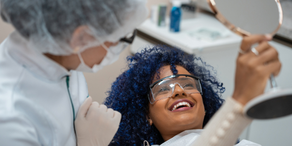 A dentist is giving a cosmetic dental treatment for a patient who is seen sitting on the chair and viewing the mirror.